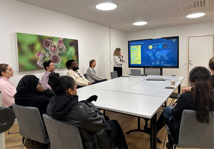 An Intertek colleague presents in front of a group of young people around a large table. 