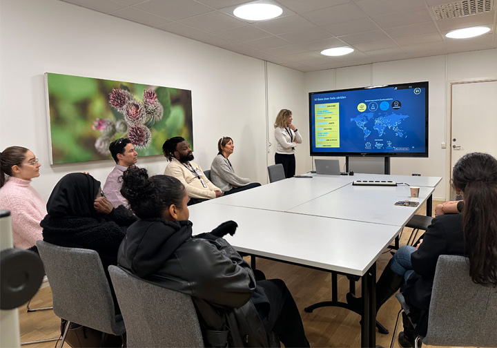 An Intertek colleague presents in front of a group of young people around a large table. 