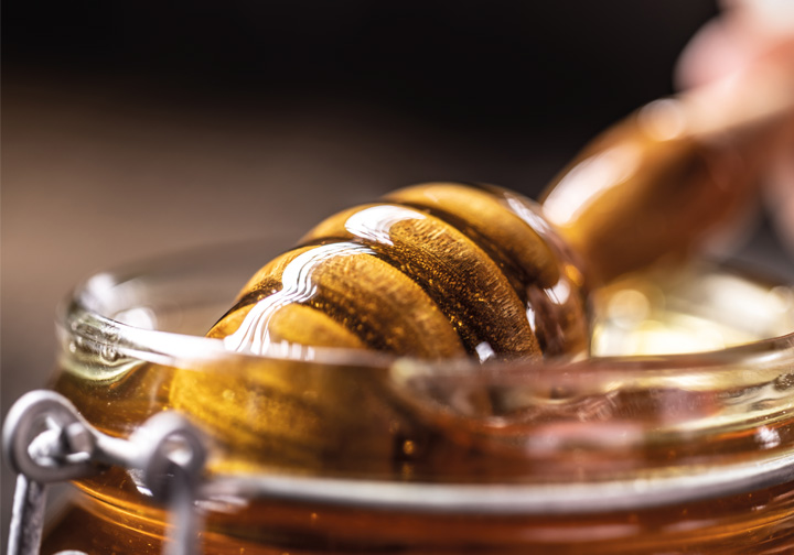 A utensil is dipped into a small glass ramekin of honey.