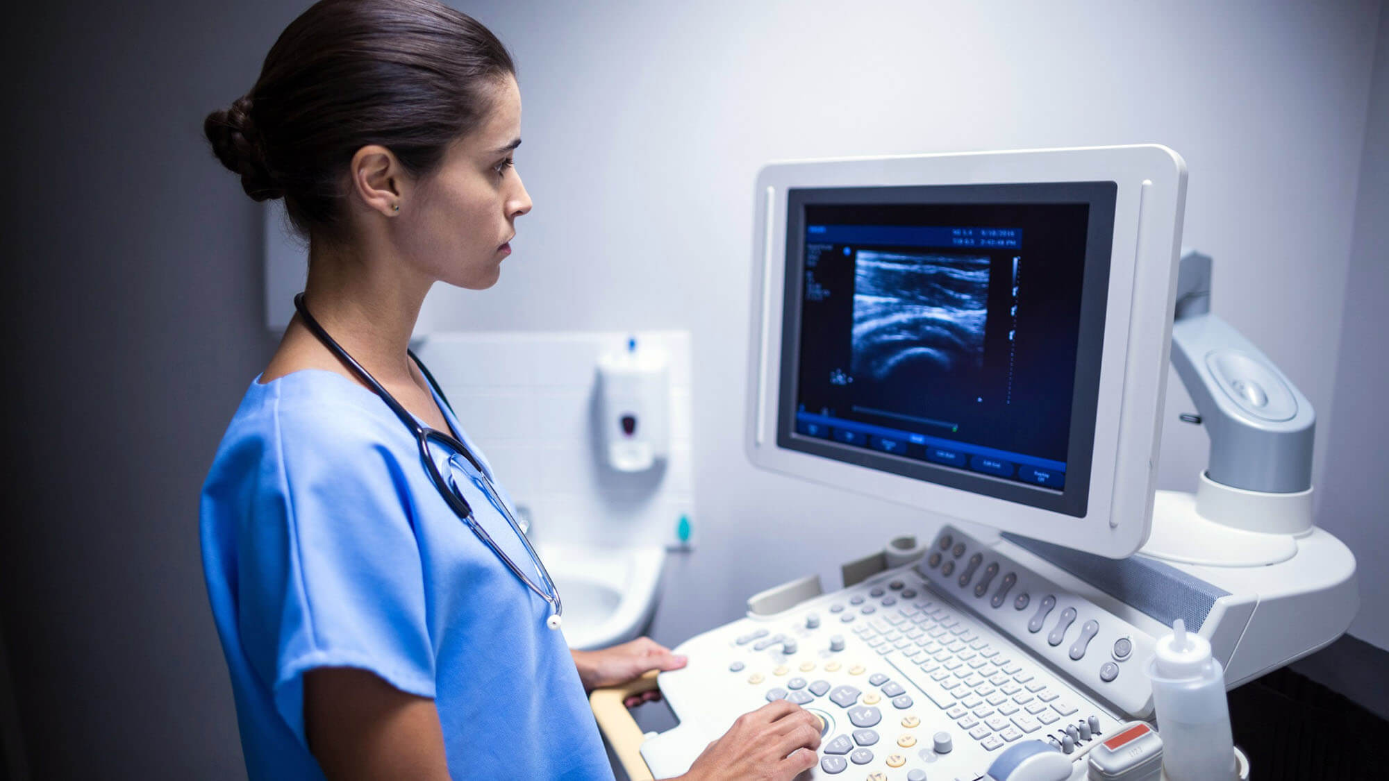 Medical professional operating an ultrasound machine with imaging displayed on the monitor.